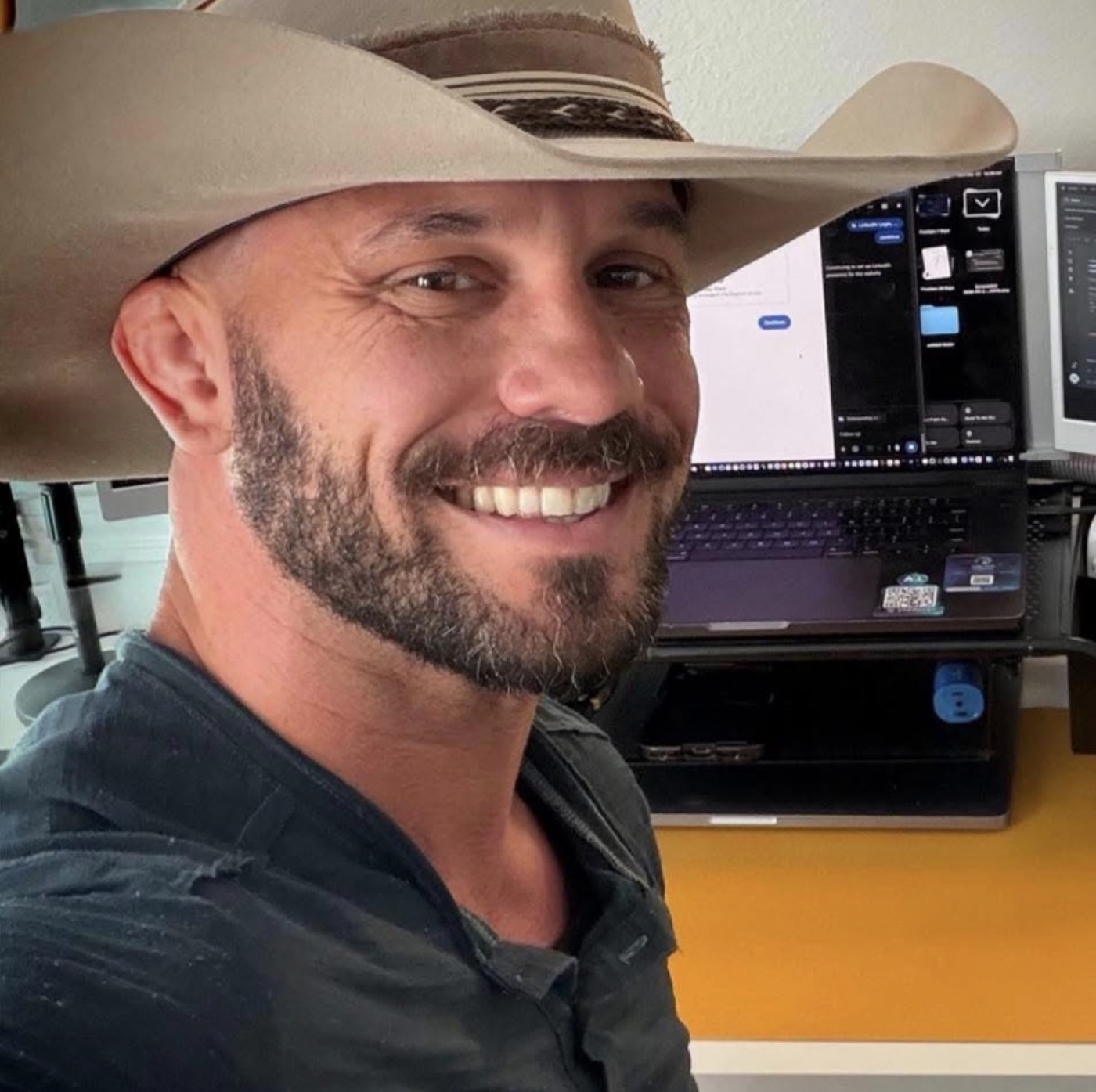 Colby Black smiling in a cowboy hat beside his computer workspace